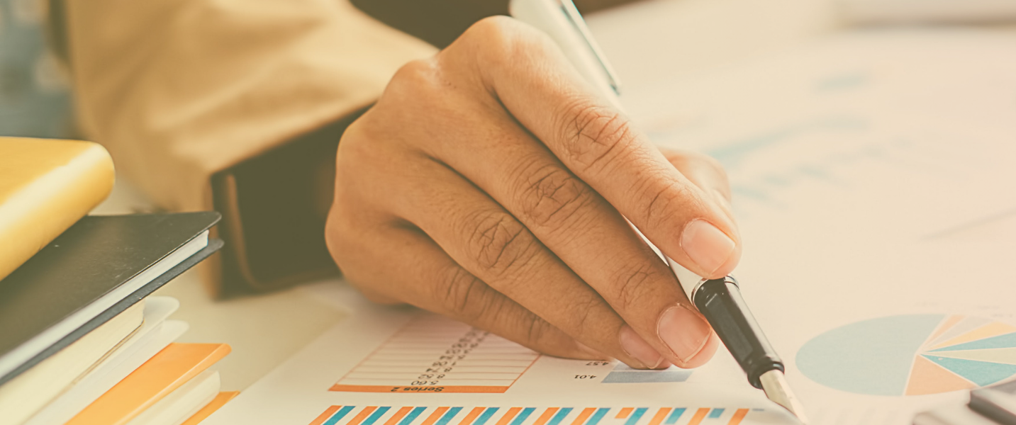 budget-planning-hand-hovers-with-pen=over-financial-report